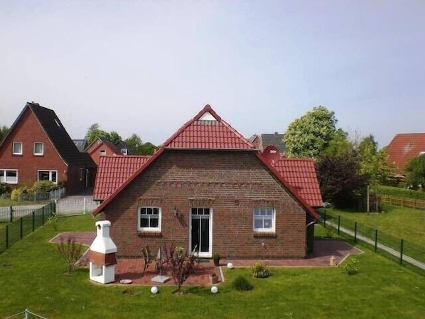 A two-story house with a red roof, a brick facade, and a small front yard with a white decorative structure.