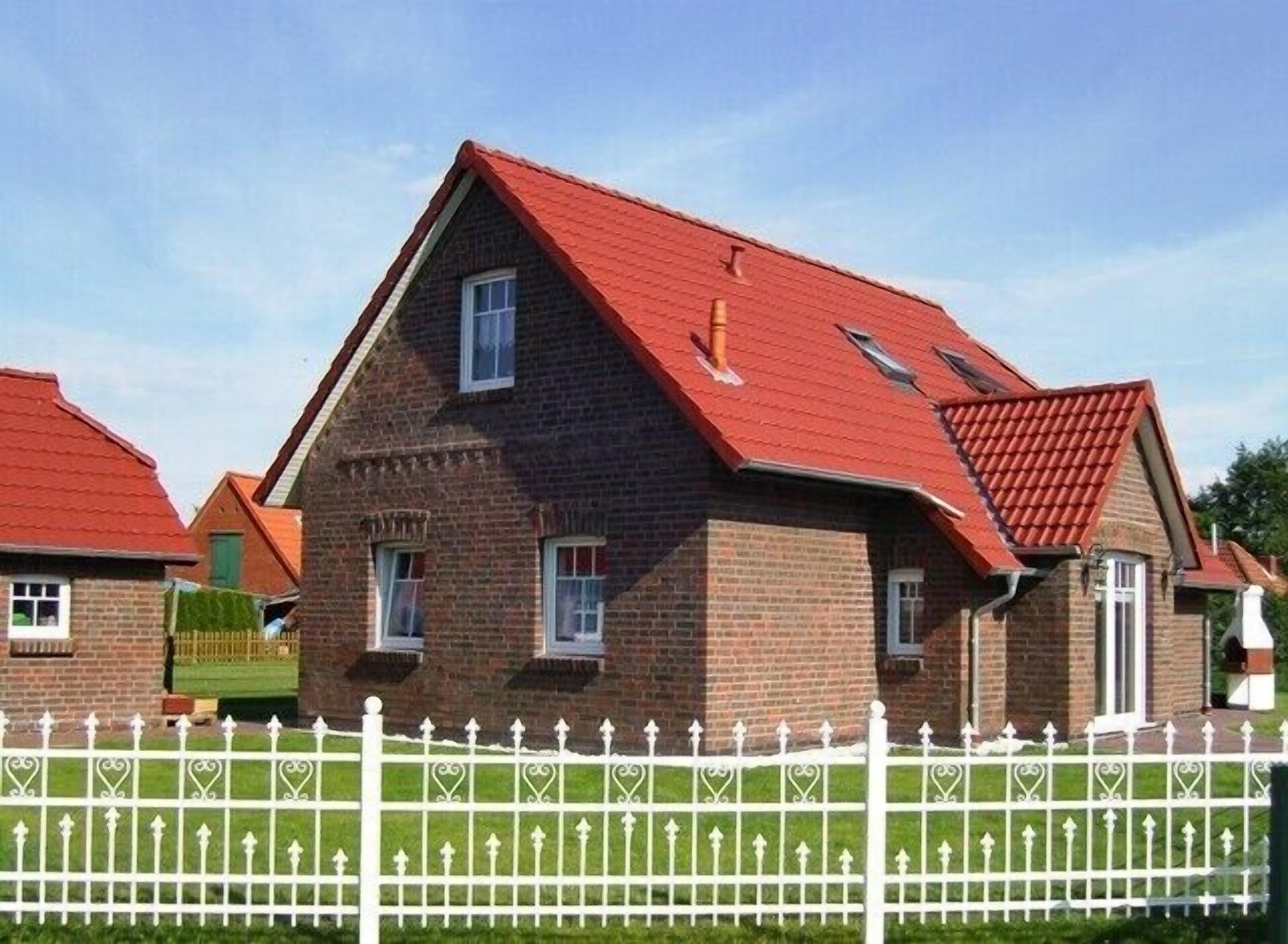 A brick house with a red roof, white picket fence, and a small garden.