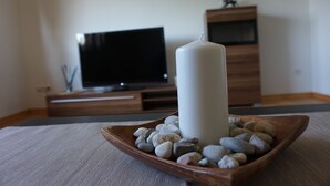 Ein Kerzenlicht auf einer Holztablett zusammen mit Kieselsteinen, einem Fernseher und Holzzimmermöbeln in einem Raum.