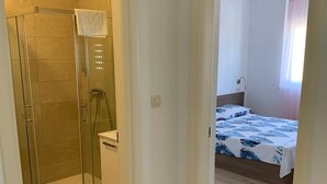 Une chambre avec une douche, un lit recouvert d’une couvre-lit à motifs et un plancher en bois.