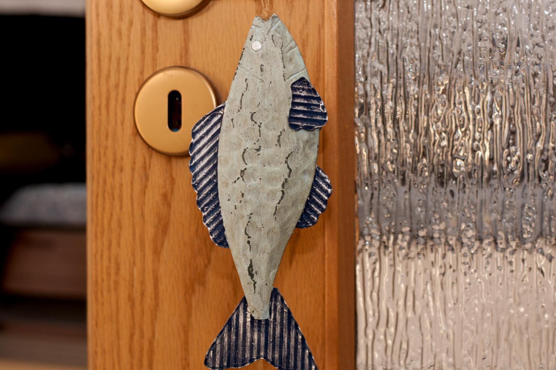 A fish-shaped door knocker on a wooden door with a round brass handle.