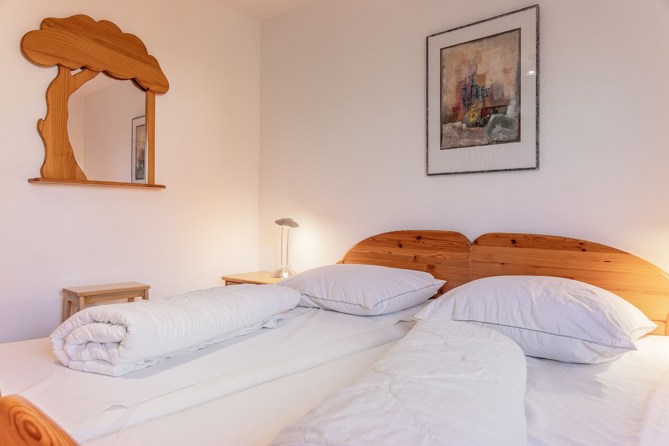 Un lit bien fait, avec du linge de lit blanc et des oreillers, une tête de lit en bois, un miroir à cadre en bois et un tableau encadré accroché au mur.