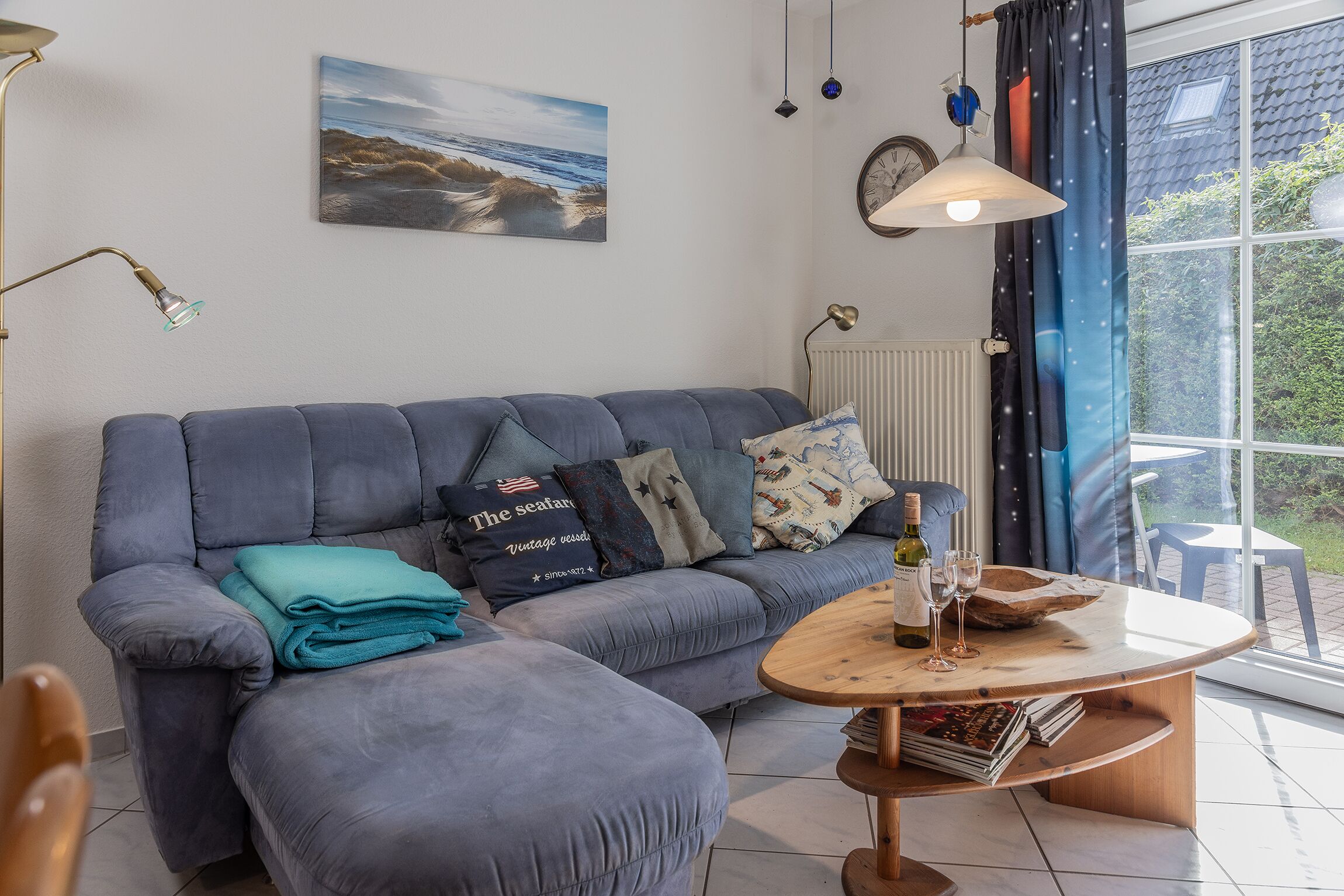 A modern living room with a grey sofa, a wooden coffee table, and a view of the outdoors through a large window.