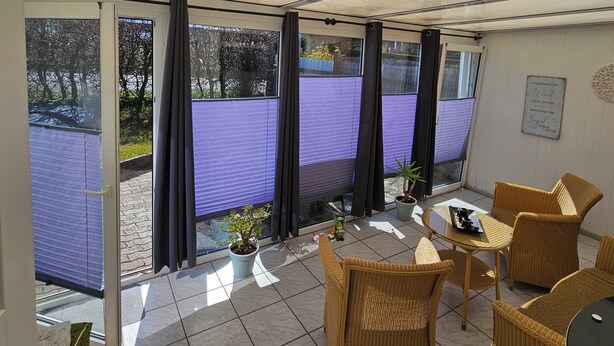 A covered outdoor area with wicker furniture, a potted plant, and a view of a purple fence. - Vacation apartment Marie in Bergen auf Rügen, quiet location (Bergen auf Rügen)