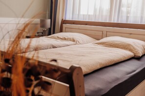 Een enkel bed met een houten hoofdbord en een donkere matras in een kamer met een raam en gordijnen.