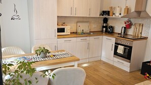A modern kitchen with white cabinets, a wooden countertop, a built-in oven, and a dining area with two chairs and a table. - Vacation apartment Marie in Bergen auf Rügen, quiet location (Bergen auf Rügen)
