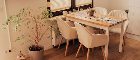 A dining area with a wooden table, four chairs, a potted plant, and a window with blinds.
