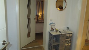 A hallway with a wooden door, a mirror on the wall, and a small table with a lamp and decorative items. - Vacation apartment Marie in Bergen auf Rügen, quiet location (Bergen auf Rügen)