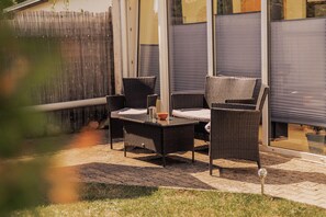 Een terras buiten met rieten meubels, een tafel en een stoel.