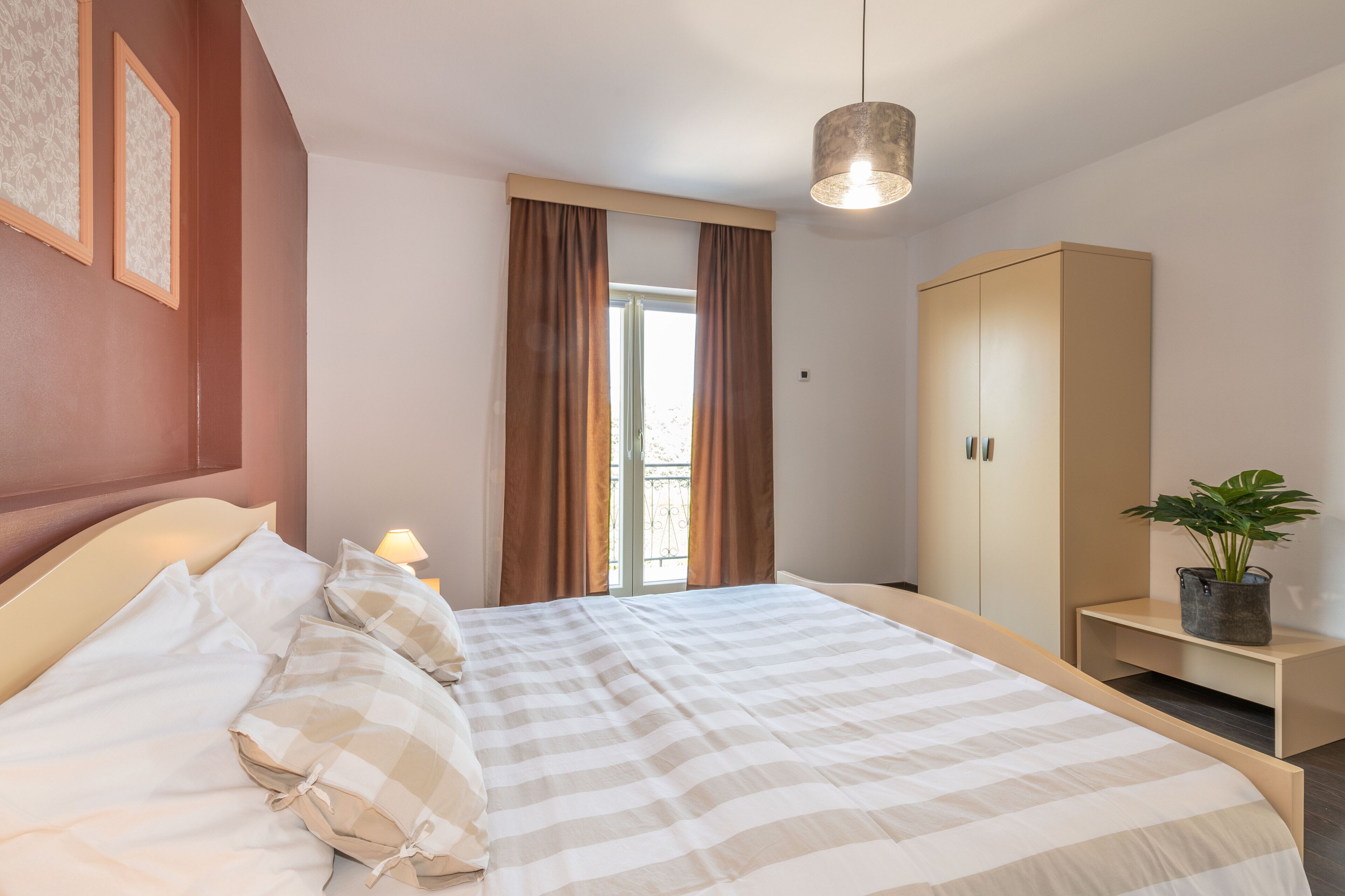 A bedroom with a bed, a wardrobe, a bedside table with a lamp, and a window with curtains.