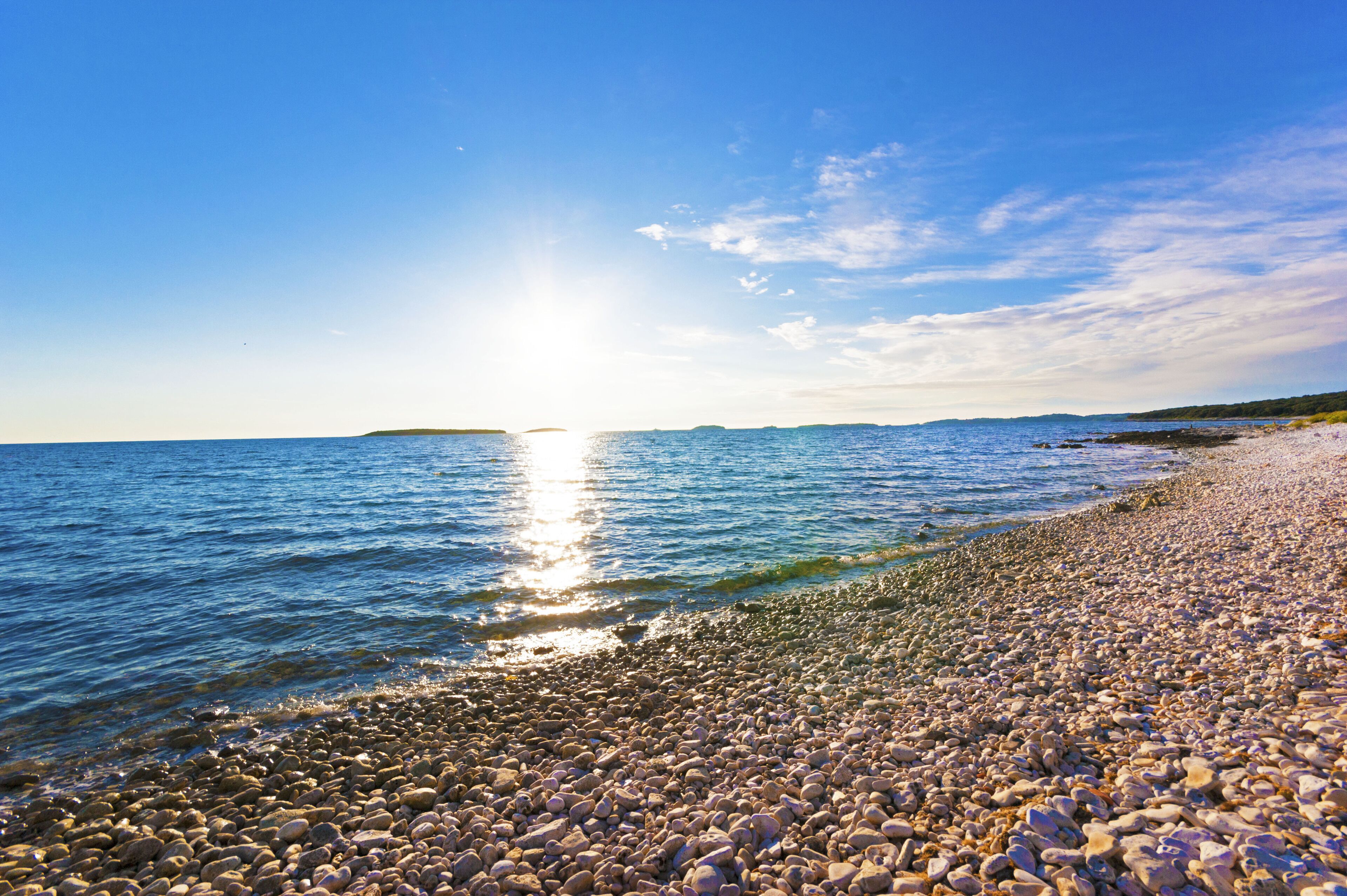 A pebbled beach with calm water and a clear sky.