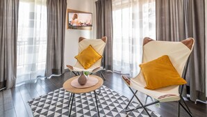 A room with two armchairs, a small table with a vase, and a TV mounted on the wall.