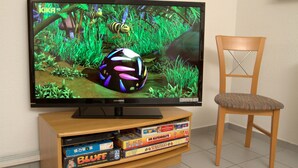 En tv-apparat som visar en färgstark animerad scen, ett träinrett möblemang för underhållning med brädspel och en trästol.