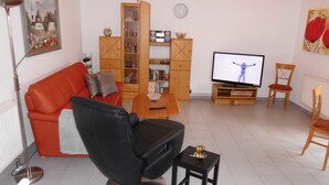 Ett vardagsrum med en röd soffa, en svart fåtölj, ett träskåp, en tv och ett litet bord med ett glas på.