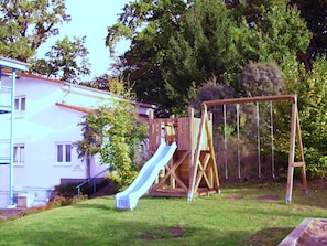 A wooden play structure with a slide and swings in a grassy yard. - Central location, south-facing balcony, own ground-floor bicycle storage room, e-car charging station. (Binz)