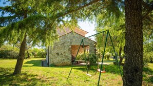 Ein Steinhaus mit einem Steindach, umgeben von Bäumen und Gras.