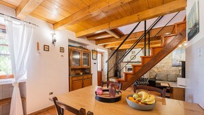 Ein Essbereich mit Holztisch, Stühlen, einer Obstschale und einer Treppe mit einer Steinwand.