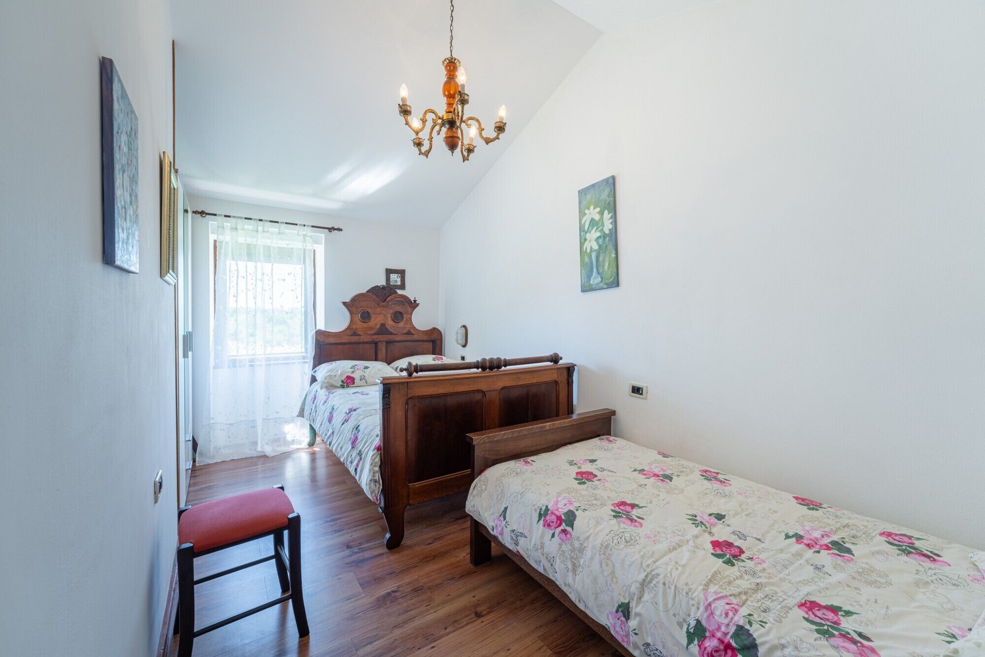 A bedroom with a wooden bed, a bench, a chandelier, and a painting on the wall.
