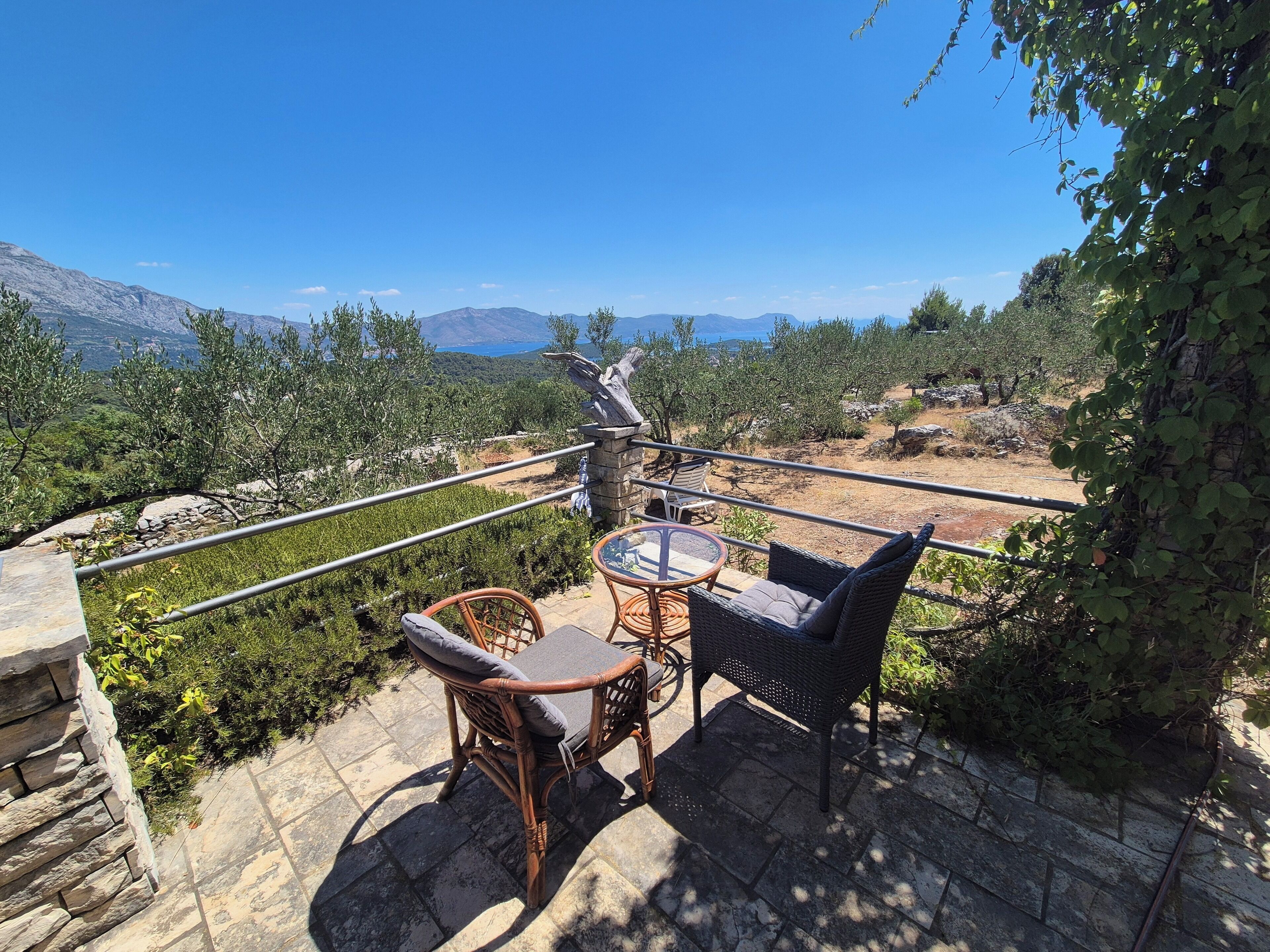 A terrace with wicker furniture and a table, overlooking a mountainous landscape.