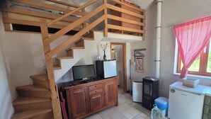 A wooden staircase leading to an upper level, a small kitchenette with a refrigerator, a television, and a cabinet.