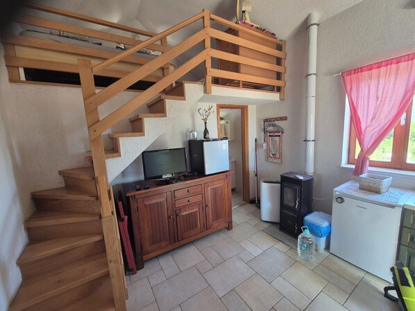 A wooden staircase leading to an upper level, a small kitchenette with a refrigerator, a television, and a cabinet.