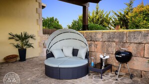 Een rond, comfortabel zitgedeelte buiten met een gebogen luifel, een barbecue en een potplant.