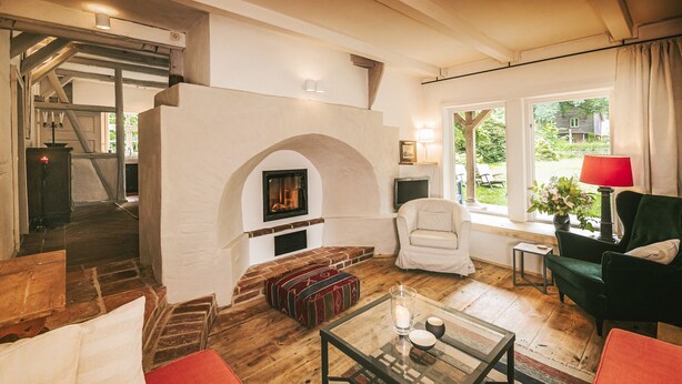 A cozy living room with a fireplace, wooden flooring, and comfortable seating. - historical house in Heidevillage on the outskirts of forest (Natendorf)