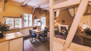 A cozy kitchen with a dining table and chairs, a fireplace, and large windows with curtains. - historical house in Heidevillage on the outskirts of forest (Natendorf)