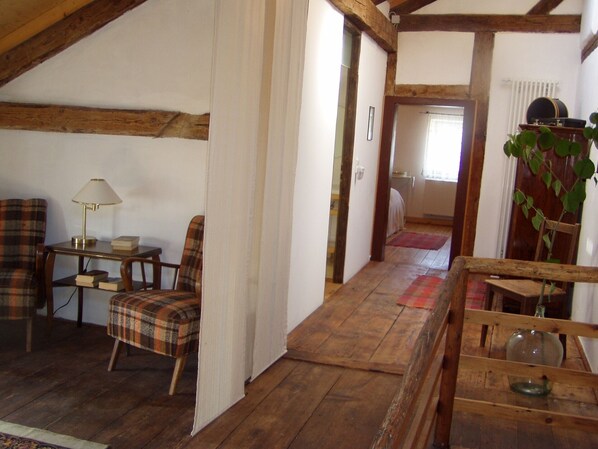 A cozy room with wooden beams, a plaid chair, a small table with a lamp, and a wooden bench with a glass bowl.