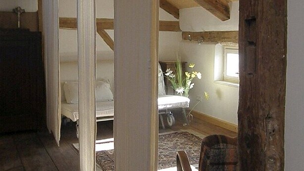 A bedroom with a bed, a window, and a wooden ceiling structure. - Living in the listed house like grandma without having to compromise on comfort (Schernfeld)