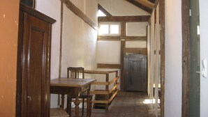 A narrow hallway with wooden beams, a wooden table with chairs, and a door on the left. - Living in the listed house like grandma without having to compromise on comfort (Schernfeld)