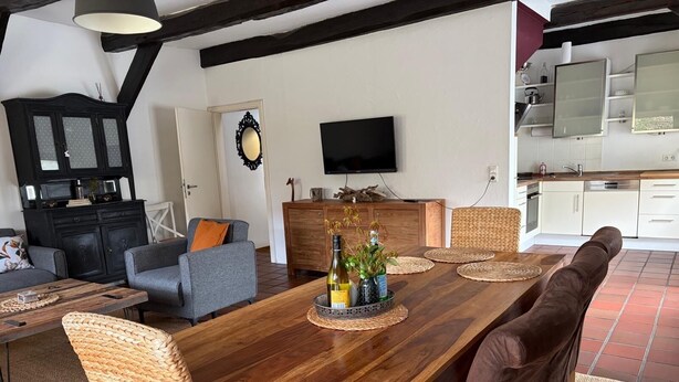 A dining area with a long wooden table, woven chairs, and a kitchen in the background. - Great facilities! Close to town! Calm! (Oldenburg)