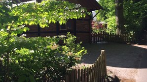 A rustic wooden cabin with a brick foundation, surrounded by lush greenery and a wooden fence. - Great facilities! Close to town! Calm! (Oldenburg)