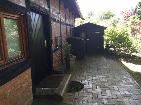 A brick building with a black door, a small porch area with a mat, and a potted plant.