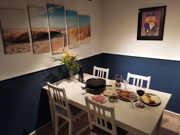 A dining table with white chairs, a vase with flowers, and various dishes including meat and vegetables. - Holiday Duinenwind - holiday in Belgium (De Haan)