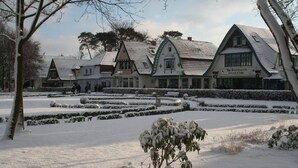 A traditional building with a snow-covered landscape, a garden with hedges, and a sign that reads "Hotel Surpach."