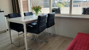 Un comedor con una mesa blanca, sillas negras y un jarrón de flores.
