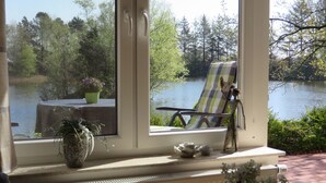 Une fenêtre donnant sur un lac, une chaise et des objets décoratifs posés sur un rebord.