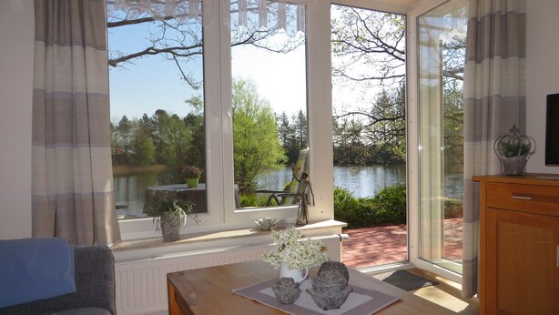Une pièce avec vue sur un lac, une table à manger agrémentée d’un vase et un canapé.