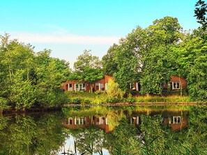 A serene lakeside setting with two brick houses surrounded by lush greenery and trees.