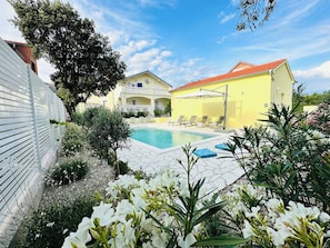 A pool area with a yellow building, white fence, and white flowers. - Private villa: 4 bedrooms, private pool (8x4m), 100m walk to the beach, sea view (Sibenik)