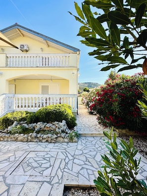 Ein zweistöckiges Gebäude mit Balkon, einem gepflasterten Eingang und einem Garten mit roten Blumen.