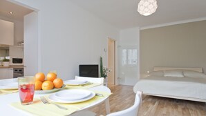 Een moderne hotelkamer met een bed, een eethoek met een tafel voor twee personen, en een keukenruimte zichtbaar door een open deur.