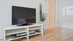 Een moderne woonkamer met een flatscreen televisie op een witte televisiemeubel, een potplant en een houten deur.