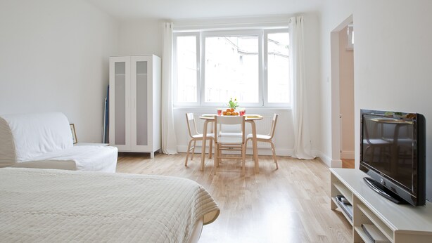 Een hotelkamer met een bed, een televisie, een eettafel met stoelen en een raam met gordijnen.