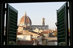 Une vue d’un bâtiment historique doté d’un dôme et d’une tour, photographiée à travers des volets ouverts.