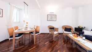 Ein modernes Wohnzimmer mit Essbereich, ausgestattet mit einem Holztisch, zwei Korbstühlen, einer Couch und einem Flachbildfernseher.