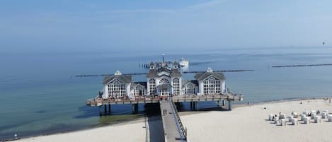 A pier extending into the water with a building at the end, featuring large windows and a balcony.