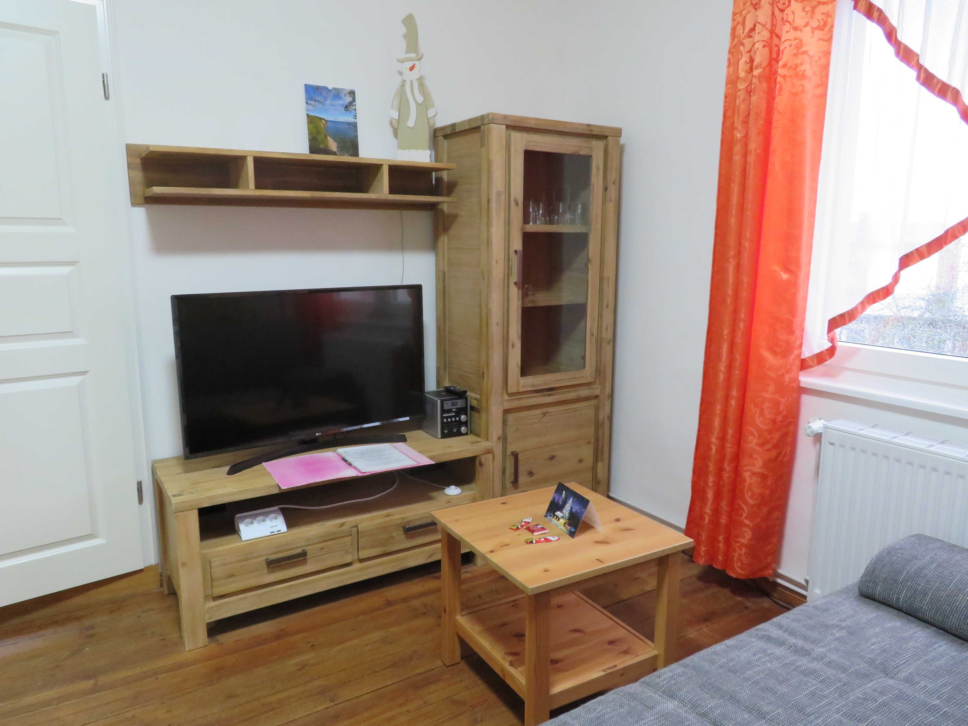 Ein Wohnzimmer mit Fernseher, Holzschrank und kleinem Tisch.