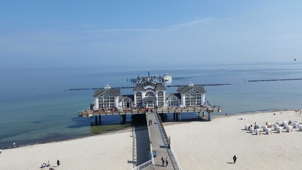 Eine Pier, die ins Wasser führt, mit einem Gebäude am Ende, das große Fenster und einen Balkon hat.